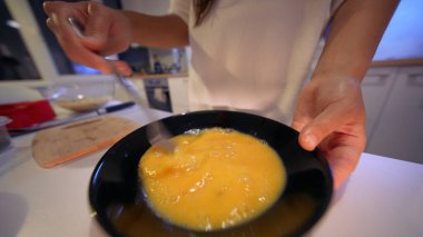 Kapalı ellerde çırpılmış yumurta kasesi, tavaya dökülmeye hazır mutfak tezgahı arka planda ve sıcak ortam aydınlatması, yemek