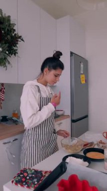 Aşçı kadın çizgili önlükle malzemeleri ölçüyor, tezgahta karıştırma kabı, cam süt kavanozu, çırpma hamuru, sakin.