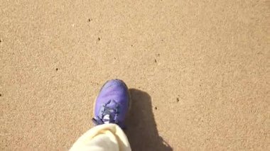 Mor spor ayakkabı kumsala basıyor, bağcıklı ayakkabı ve taban izine yakın çekim, gölge çizgisi ve günlük pantolon, düzgün adımlar.,