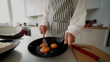 Tezgahta omlet için yumurta çırpan beyaz kadın, kıvrımlı siyah kase sarısı, ahşap tahta ve bıçak.,