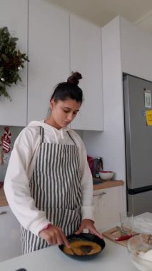 Mutfak kadını siyah tavada kalın hamuru karıştırıyor. Spatula, çizgili önlük ve rahat çelenk ile yavaş dairesel hareket ediyor.,