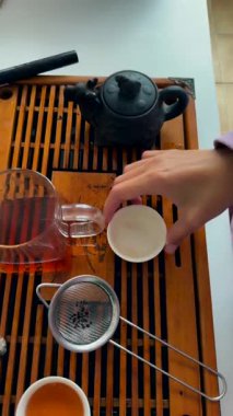 Ahşap tepside çaydanlık yakalayan telefon, kadın elleri döşeme ve süzgeç, kehribar çayına yakın çekim, sıcak mutfak ışığı ve samimi