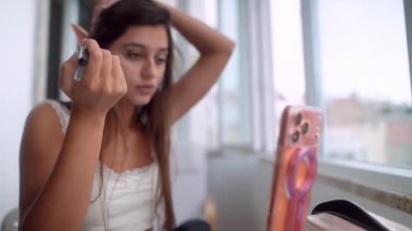 Genç yaşlı kadın saçını geriye çekiyor ve son rimel sürüşünü yapıyor. Pencere kenarına dokunuyor. Kendine güveni tam, aynayla ortaya çıkıyor.