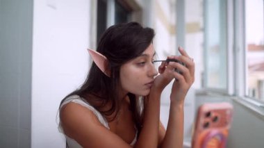 Yaşlı kadın küçük aynayı kontrol ediyor ve pencerede hassas bir rötuş yapıyor, kirpik ve kalas işi, olay öncesi ışıltı oluşturdu