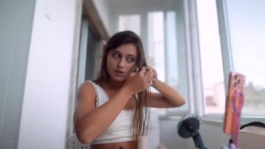 Balkonda genç bir kadın saç ve elf kulağı aksesuarı, telefon standı, makyaj masasına saçılmış, niyet ifadesi.