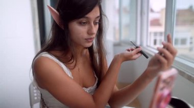 Gösteriş için maskara ve makyaj yaparken gülümseyen genç, yaşlı bir kadın. Akıllı telefon kamerasıyla neşeli bir içerik anı.,