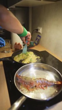 Paslanmaz tavada cızırdayan karides, yeşil bileklik takan beyaz aşçı, yakınlarda kızarmış pirinç, tereyağında kavrulmuş büyük çiğ karides.