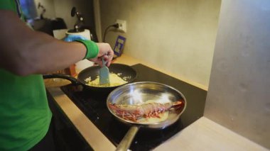 Ev yapımı yumurta ve karides, yeşil gömlekli ve bileklikli indüksiyon sobası, spatula kullanan yakın çekim eller, domuz pastırması.