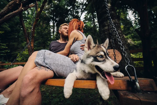Beautiful couple together with dog on a swing — Stock Photo, Image