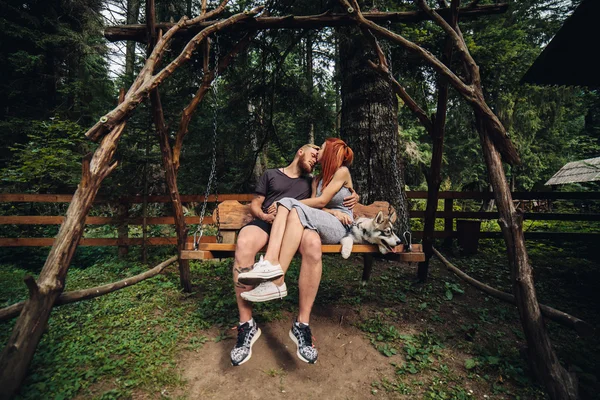 Beautiful couple together with dog on a swing — Stock Photo, Image