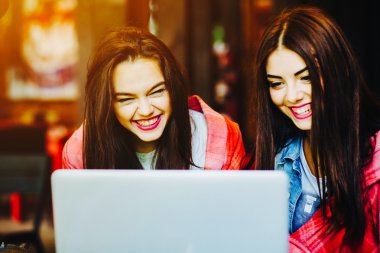 İki kız dizüstü bilgisayarda bir şey izliyor.