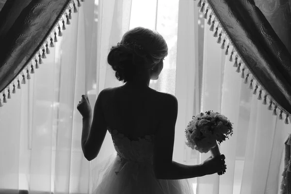 Beautiful bride in a wedding dress, by window. — Stock Photo, Image