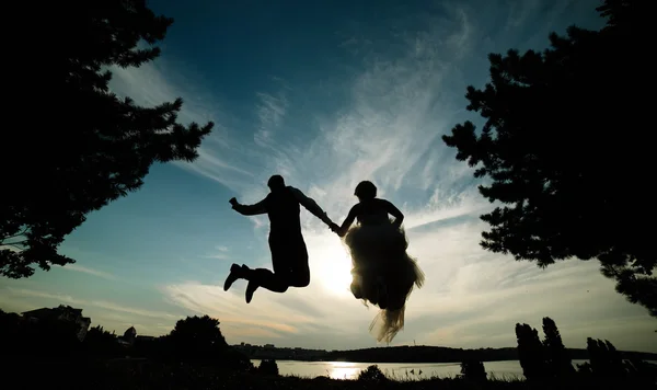 Novio y novia saltando contra el hermoso cielo — Foto de Stock