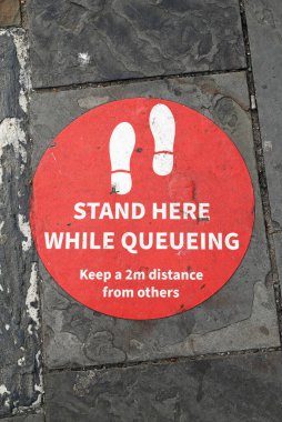 İngiltere, Weston-super-Mare 'de bir kaldırıma şablonla yazılmış bir tabela, iki metre uzakta durmaları için kuyrukta bekleyenleri uyarıyor.