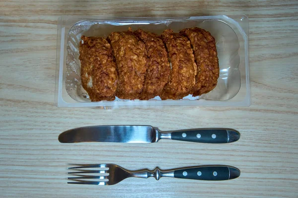 Tahta bir masada çatal ve bıçakla servis edilen paketlenmiş domuz pirzolası..