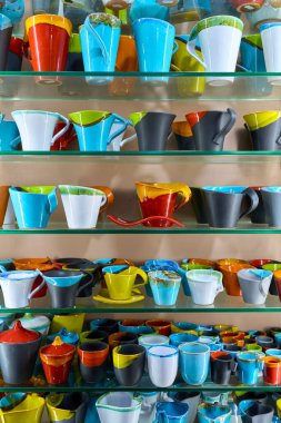 Çömlekçide renkli el yapımı seramik bardaklar ve kupalarla dolu raflar. Parlak bir iç perakende satışta canlı, cam kaplı sofra takımı, zanaatkarlık, yaratıcı tasarım ve yaşam tarzı dekorasyonu sergiliyor..