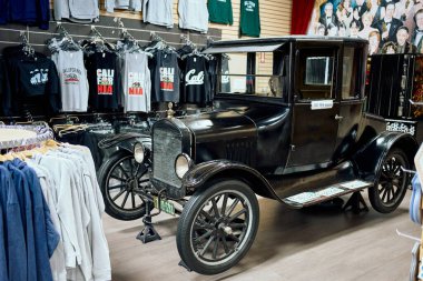 20. yüzyılın başlarında Kaliforniya grafik tişörtleriyle çevrili bir hediyelik eşya ve giysi dükkanında sergilenen klasik siyah otomobil. Modern perakende ile otomotiv geçmişini harmanlayan klasik araba sergisi.
