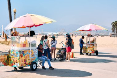 Los Angeles sahillerinde taze meyve satan sokak yemekleri satıcıları. Renkli şemsiyeler, dinlenen insanlar, ve ikonik Kaliforniya plaj yaşam tarzı ve yaz tatili atmosferi..