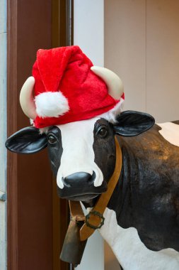 Noel süsü olarak Noel Baba şapkası takan komik inek heykeli. Çiftlik hayvanı, şenlik havası ve kış kutlaması temalı komik bir tatil konsepti..