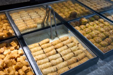 Fırın tezgahındaki metal tepsilerde geleneksel baklava hamur işleri. Filo pastası, bal şurubu ve fındık ile yapılan Orta Doğu ve Akdeniz tatlıları, bir şekerleme vitrininde yeni hazırlanmış tatlılar..