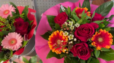 Kırmızı güller, gerbera papatyaları ve dekoratif ambalajda yeşillik içeren iki çiçek buketinin yakın çekimi. Hediyeler ve kutlamalar için çiçekçide sergilenen taze çiçek aranjmanları..