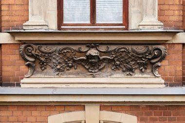 Melek yüzlü dekoratif taş döşeme, çiçek süsleri ve pencerenin altındaki kaydırma. Geleneksel tuğla bina dış yüzeyi üzerine detaylı mimari öğe.