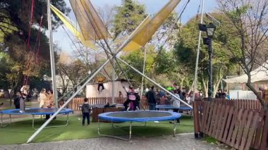 Çocuklar açık hava parkında koşum takımlarıyla bungee trampolinlerde zıplıyorlar. Trampolinlerle, güvenlik halatlarıyla ve destek yapısıyla aile eğlencesi. Boş zaman, eğlence ve eğlence konsepti..