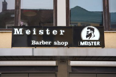 Bay Berber Dükkanı tabelası binanın ön cephesine asılmış. Girişin üzerinde beyaz harfler ve logo bulunan siyah vitrin levhası..