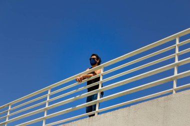 Maske takmış, korkuluklara tutunmuş, alt kattan görülmüş..