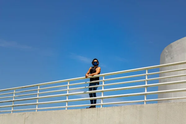 Man, wearing a mask, propped up on a railing parapet seen from the lower floor.