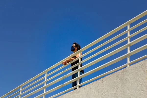 Man, wearing a mask, propped up on a railing parapet seen from the lower floor.