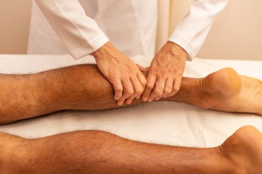 Sedyede yatan hastaya bacak masajı yapan bir terapist..