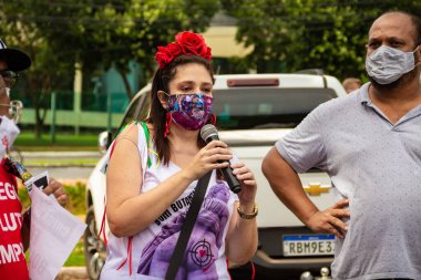 Bolsonaro 'nun görevden alınması için gösteri çağrısı. Saçında çiçekler olan ve maske takan bir kadın, protesto etmek için mikrofona konuşuyor..