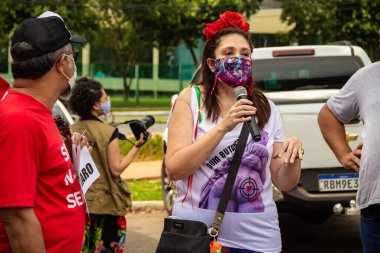 Bolsonaro 'nun görevden alınması için gösteri çağrısı. Saçında çiçekler olan ve maske takan bir kadın, protesto etmek için mikrofona konuşuyor..