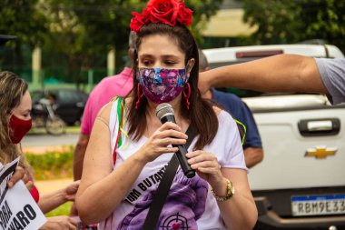 Bolsonaro 'nun görevden alınması için gösteri çağrısı. Saçında çiçekler olan ve maske takan bir kadın, protesto etmek için mikrofona konuşuyor..