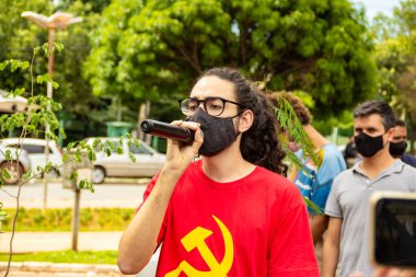 Kırmızı bluzlu ve siyah maskeli çocuk protestoda mikrofona konuşuyor. Brezilya Başkanı 'nın görevden alınmasını talep ediyor..