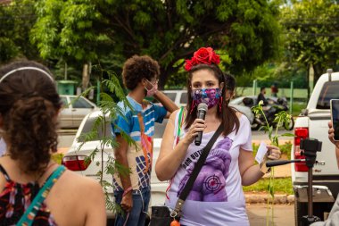 Bolsonaro 'nun itham edilmesini talep eden bir gösteri. Saçında çiçekler olan, maskeli bir kadın, protesto etmek için mikrofona konuşuyor..