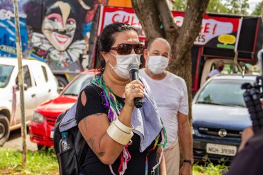 Kadın, maske takıyor, Goinia 'da kültürel profesyonellerin protestosu sırasında mikrofona konuşuyor..