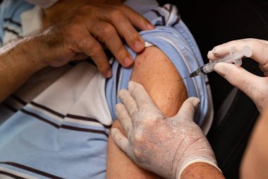 Arabanın içindeki yaşlı adam araba sürerken aşı oluyor..