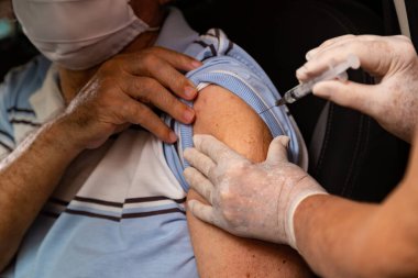 Arabanın içindeki yaşlı adam araba sürerken aşı oluyor..