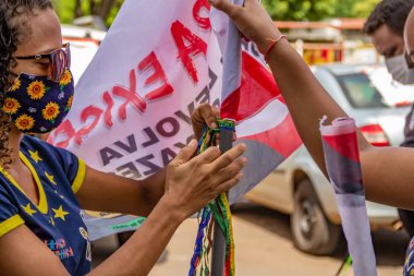 Goinia şehrinde kültürel profesyonellerin gösterisi için bayrak direğine renkli kurdele bağlayan iki genç kadın..