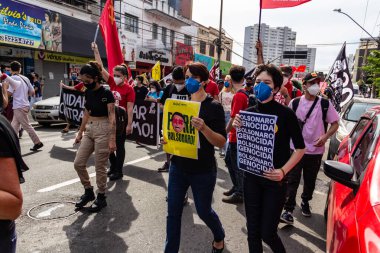 Protestocular gösteride maske takıp tabela tutuyorlar. Protesto; Brezilya Cumhurbaşkanı Bolsonaro 'ya karşı düzenlenen bir protesto sırasında çekilen fotoğraf ve nüfusu bağışık hale getirmek için aşı satın almada çeviklik istenmesi.