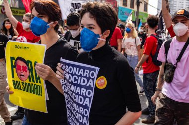 Protestocular gösteride maske takıp tabela tutuyorlar. Protesto; Brezilya Cumhurbaşkanı Bolsonaro 'ya karşı düzenlenen bir protesto sırasında çekilen fotoğraf ve nüfusu bağışık hale getirmek için aşı satın almada çeviklik istenmesi.