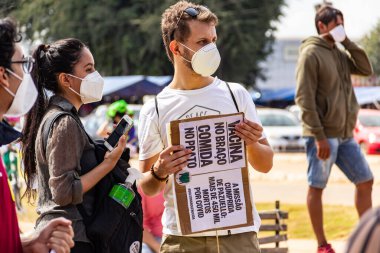 Protestocu maske takıyor ve protesto için pankart tutuyor. Protesto; Brezilya Cumhurbaşkanı Bolsonaro 'ya karşı düzenlenen bir protesto sırasında çekilen fotoğraf ve nüfusu bağışık hale getirmek için aşı satın almada çeviklik istenmesi.