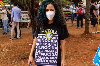 Protestocu maske takıyor ve protesto için pankart tutuyor. Protesto; Brezilya Cumhurbaşkanı Bolsonaro 'ya karşı düzenlenen bir protesto sırasında çekilen fotoğraf ve nüfusu bağışık hale getirmek için aşı satın almada çeviklik istenmesi.