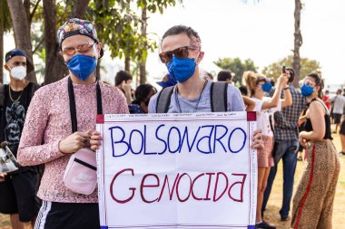 Protestocu maske takıyor ve protesto için pankart tutuyor. Protesto; Brezilya Cumhurbaşkanı Bolsonaro 'ya karşı düzenlenen bir protesto sırasında çekilen fotoğraf ve nüfusu bağışık hale getirmek için aşı satın almada çeviklik istenmesi.