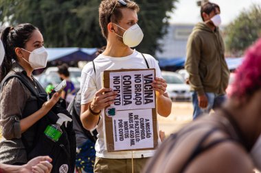 Protestocu maske takıyor ve protesto için pankart tutuyor. Protesto; Brezilya Cumhurbaşkanı Bolsonaro 'ya karşı düzenlenen bir protesto sırasında çekilen fotoğraf ve nüfusu bağışık hale getirmek için aşı satın almada çeviklik istenmesi.