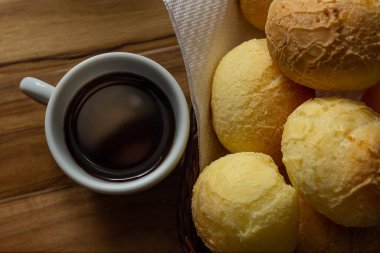 Bir fincan kahve ve peynirli çörek. Peynir ekmeği dolu küçük bir hasır sepet ve tahtadan bir yüzey üzerinde kahve olan beyaz bir fincan. Kahvaltı..