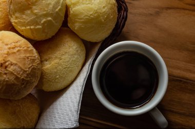 Bir fincan kahve ve peynirli çörek. Peynir ekmeği dolu küçük bir hasır sepet ve tahtadan bir yüzey üzerinde kahve olan beyaz bir fincan. Kahvaltı..