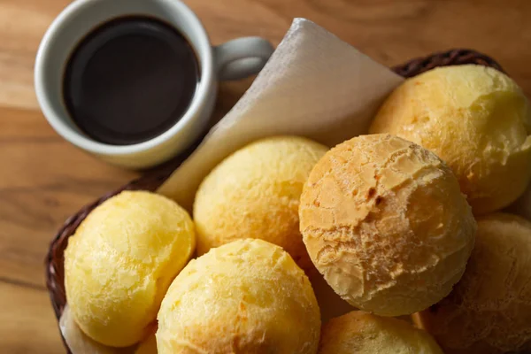 Bir fincan kahve ve peynirli çörek. Peynir ekmeği dolu küçük bir hasır sepet ve tahtadan bir yüzey üzerinde kahve olan beyaz bir fincan. Kahvaltı..